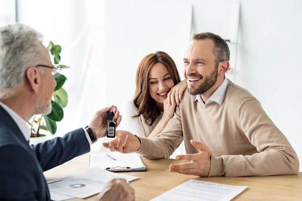Selective focus of cheerful man looking at car dealer holding car key — Stock Photo