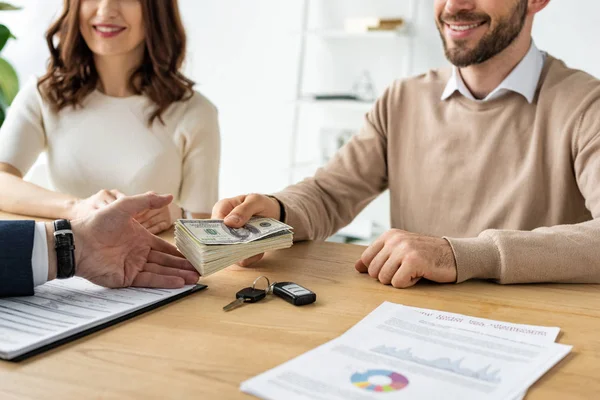 Cropped view of happy man giving dollar banknotes to car dealer near cheerful woman — Stock Photo