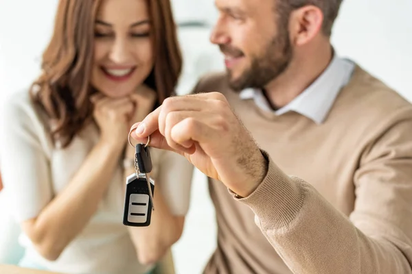 Selektiver Fokus eines gutaussehenden Mannes mit Autoschlüssel und Blick auf eine glückliche brünette Frau — Stockfoto