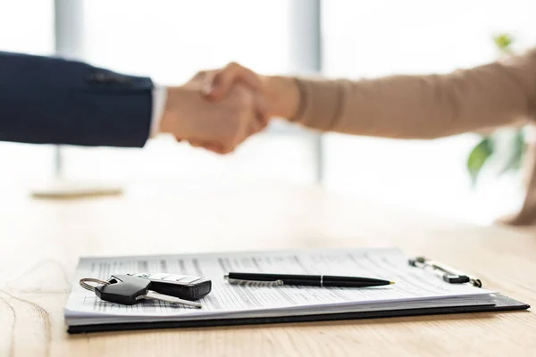 Selective focus of clipboard, pen and car key near men shaking hands — Stock Photo