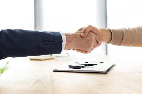 Selective focus of man and car dealer shaking hands near clipboard, pen and car key — Stock Photo