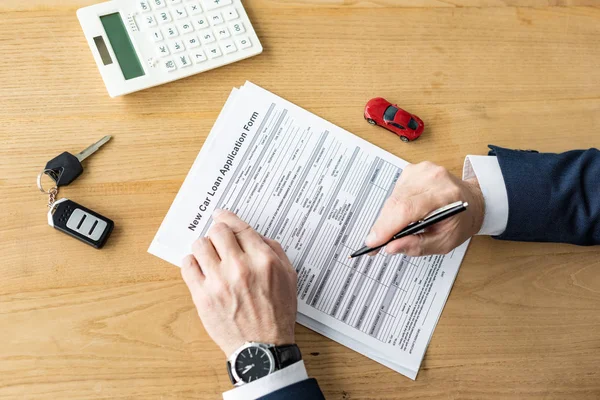 Vue recadrée du concessionnaire automobile tenant le stylo près du contrat, calculatrice, voiture jouet et clé de voiture — Photo de stock