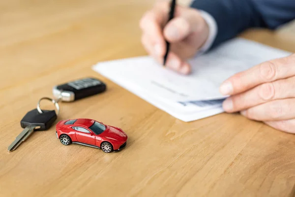 Foco seletivo do carro de brinquedo vermelho perto da chave do carro e do negociante do carro que prende a pena perto do contrato — Fotografia de Stock