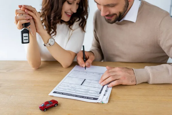 Enfoque selectivo del hombre barbudo firma contrato cerca de la mujer que sostiene la llave del coche - foto de stock