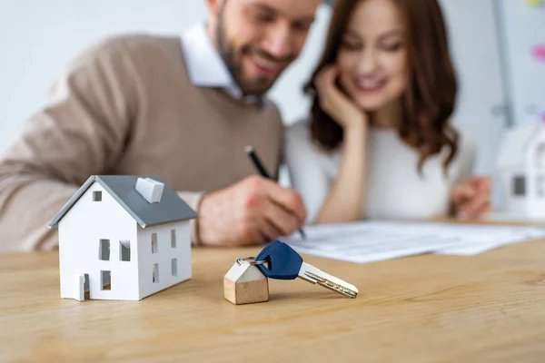 Selective focus of house model and keys near happy man and woman — Stock Photo