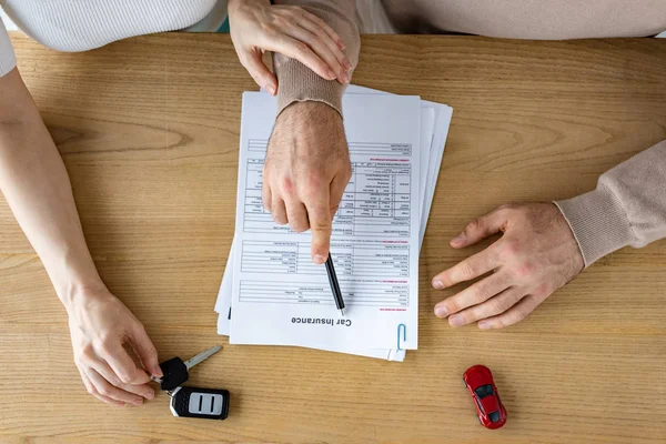 Vista dall'alto dell'uomo che tiene la penna vicino al documento con iscrizione di assicurazione auto e donna — Foto stock
