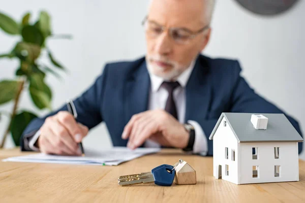 Selective focus of keys and house model near house dealer in glasses — Stock Photo