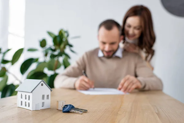 Selective focus of toy house and keys near happy man and woman — Stock Photo