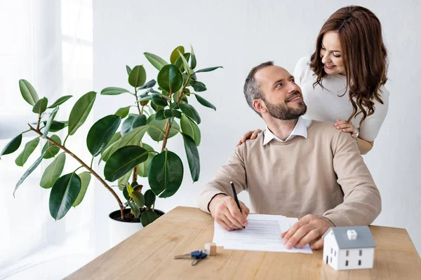 Selective focus of bearded man looking at happy woman near house model and keys on table — Stock Photo