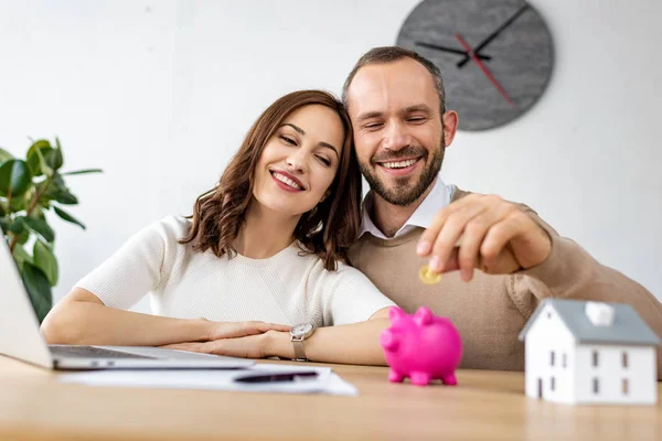 Selective focus of happy man putting golden coin in pink piggy bank near attractive woman — Stock Photo