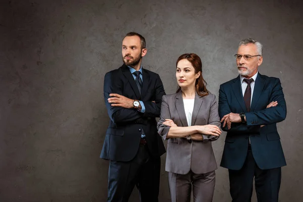 Exitosa mujer de negocios y hombres de negocios guapos de pie con los brazos cruzados en gris - foto de stock