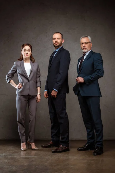 Low angle view of businesswoman standing with hand on hip near handsome businessmen on grey — Stock Photo