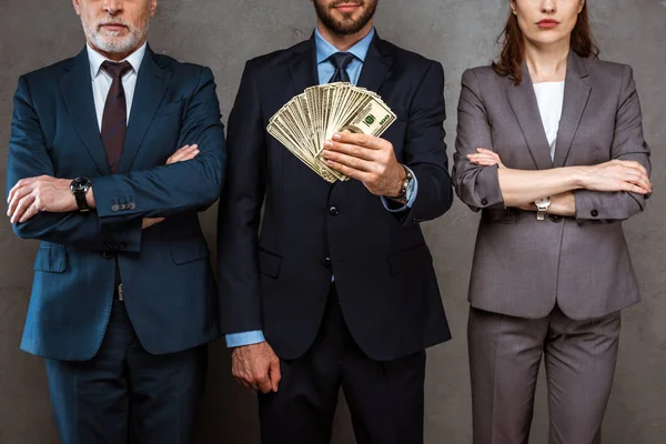 Vista recortada del hombre de negocios sosteniendo billetes de dólar cerca de socios en gris - foto de stock