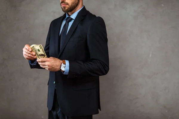 Vue recadrée d'un homme d'affaires barbu tenant des billets en dollars sur fond gris — Photo de stock