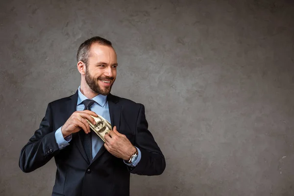 Happy businessman putting dollar banknotes in pocket on grey — Stock Photo