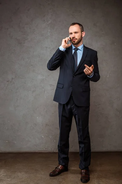 Homem de negócios bonito falando no smartphone e apontando com o dedo no cinza — Fotografia de Stock
