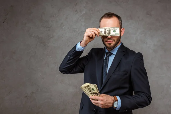 Homme d'affaires en costume couvrant les yeux avec un billet en dollar sur gris — Photo de stock