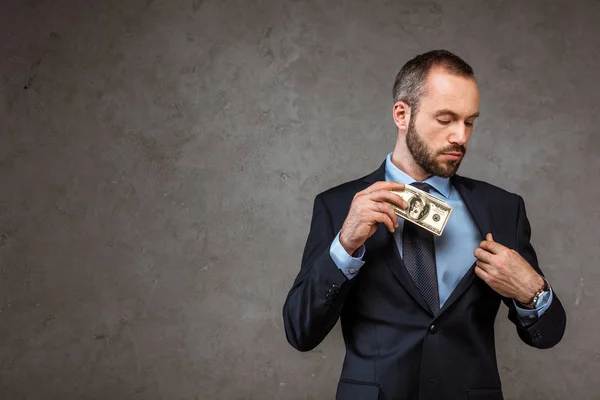 Exitoso hombre de negocios poniendo billetes de dólar en el bolsillo en gris - foto de stock