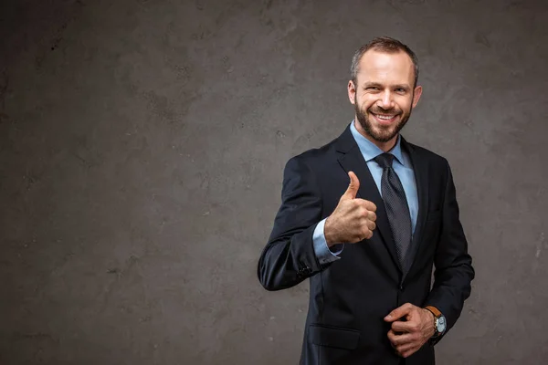 Щасливий бородатий бізнесмен у костюмі показує великий палець на сірому — стокове фото