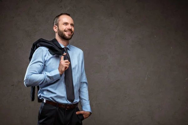 Cheerful businessman standing with hand in pocket and smiling on grey — Stock Photo