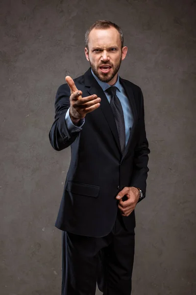 Wütender bärtiger Geschäftsmann im Anzug gestikuliert auf grau — Stockfoto