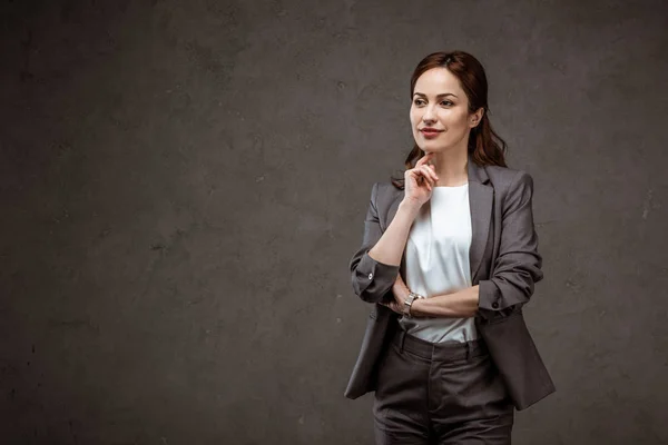 Nachdenkliche brünette Geschäftsfrau steht und denkt auf grau — Stockfoto