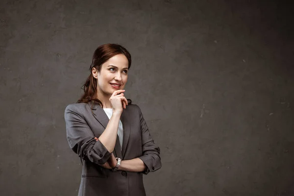 Стомлена брюнетка бізнес-леді посміхається, стоячи на сірому — стокове фото