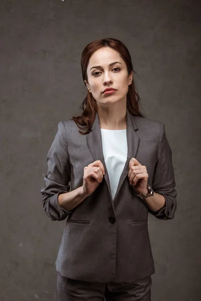 Atractiva mujer de negocios morena en ropa formal mirando a la cámara en gris - foto de stock