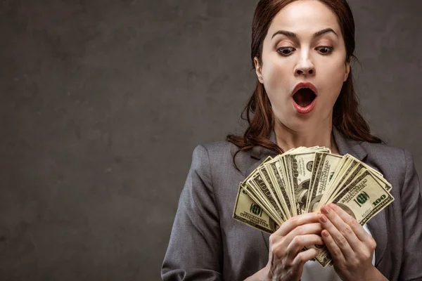 Shocked brunette businesswoman looking at dollar banknotes on grey — Stock Photo