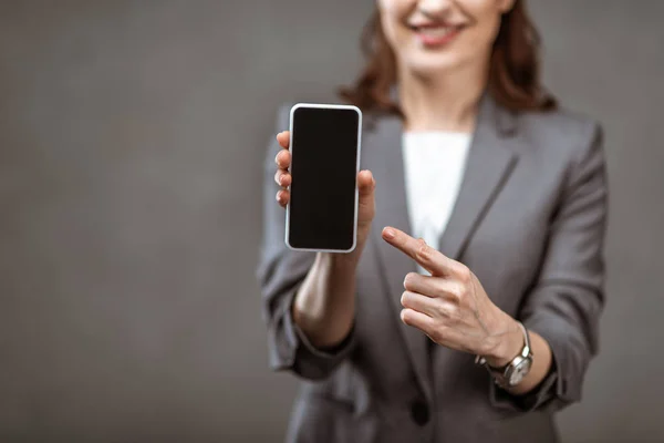 Selektiver Fokus der Geschäftsfrau, die mit dem Finger auf Smartphone mit leerem Bildschirm auf grau zeigt — Stockfoto