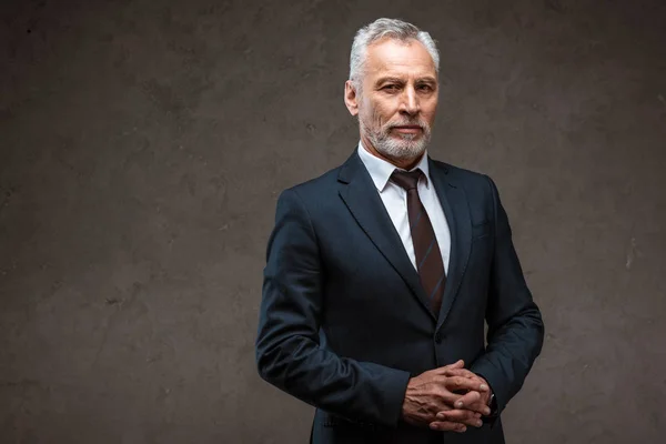 Успішний бізнесмен у костюмі, що стоїть зі згорнутими руками на сірому — стокове фото