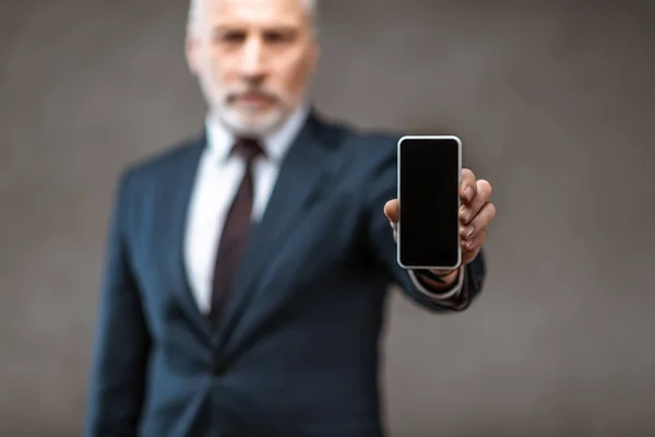 Selective focus of businessman holding smartphone with blank screen on grey — Stock Photo