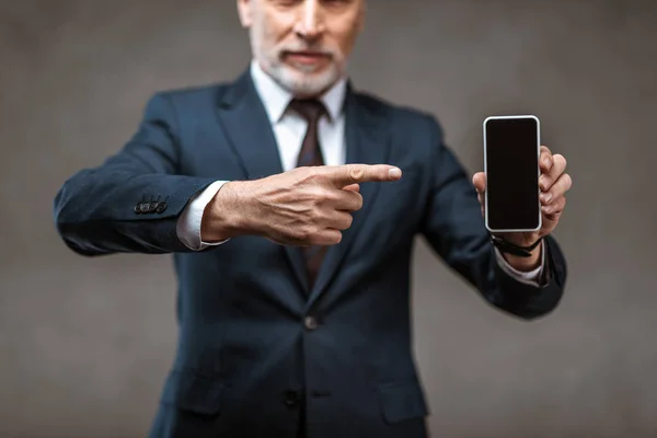 Selective focus of businessman pointing with finger at smartphone with blank screen on grey — Stock Photo