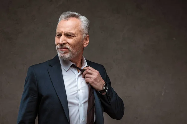 Hombre de negocios disgustado en traje tocando corbata en gris - foto de stock