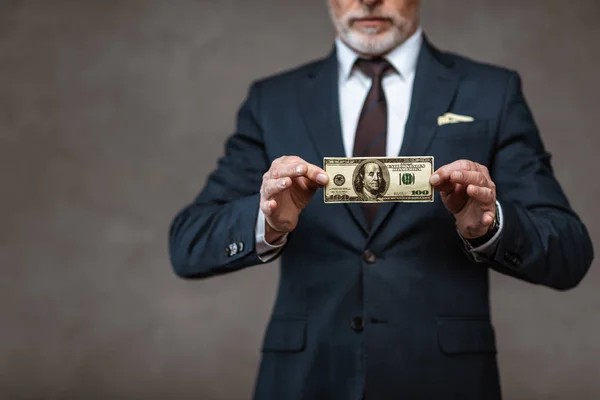 Обрезанный взгляд бизнесмена, держащего долларовую банкноту на сером — стоковое фото
