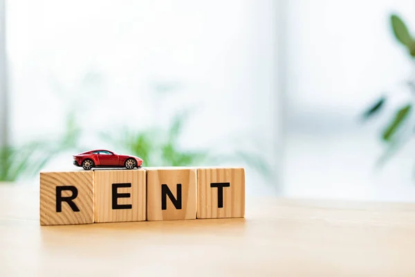 Coche de juguete rojo en cubos de madera con letras de alquiler en la mesa - foto de stock