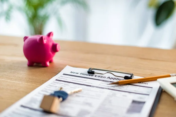 Selective focus of clipboard with new house loan lettering on document near keys, pencil  and pink piggy bank — Stock Photo