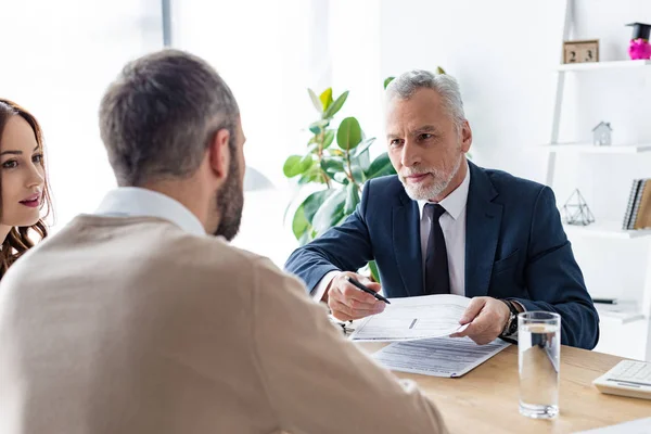 Selective focus of car dealer in formal wear giving pen and contract to man near attractive woman — Stock Photo