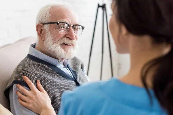 Selective focus of cheerful and grey haired man looking at nurse — Stock Photo