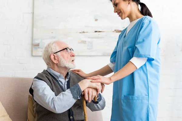Side view of elderly man and nurse standing in room, looking at each other — Stock Photo