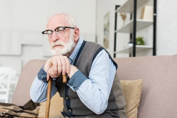 Bärtiger und grauhaariger Mann sitzt im hellen Raum und legt die Hände auf den Gehstock — Stockfoto