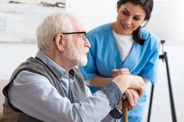 Selektiver Fokus eines ruhigen grauhaarigen Mannes, der auf einer Couch sitzt, in der Nähe einer lächelnden Krankenschwester — Stockfoto