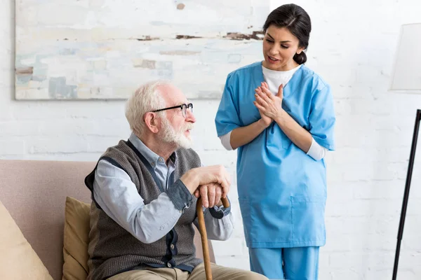 Enfermera hablando con el hombre mayor barbudo, de pie dentro de la habitación luminosa - foto de stock