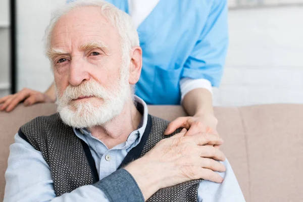 Обрезанный вид медсестры, стоящей позади пожилого человека, кладущей руку ему на плечо — стоковое фото