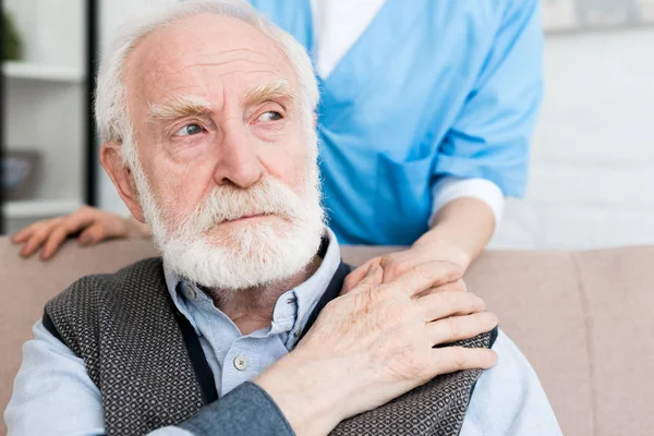 Nurse putting hand on sad and grey haired patient — Stock Photo