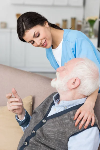 Enfermera sonriente poniendo las manos en el hombre de pelo gris - foto de stock