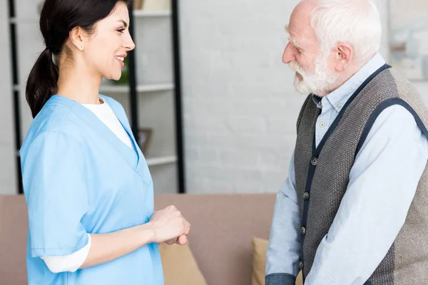 Side view of elderly man standing in room, looking at smiling doctor — Stock Photo