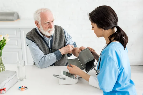Медсестра вимірює кров'яний тиск бородатого сірого волосатого чоловіка — стокове фото