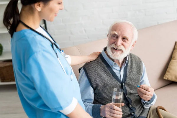 Высокий угол обзора медсестры положить руки на счастливый седой мужчина с таблетками — стоковое фото