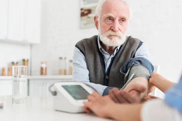 Вибірковий фокус спокійного сірого волосистого чоловіка, який дивиться геть, а жінка вимірює кров'яний тиск — стокове фото